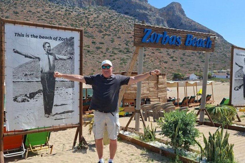 A man standing in front of a beach sign with a photo of a man on the beach. 1