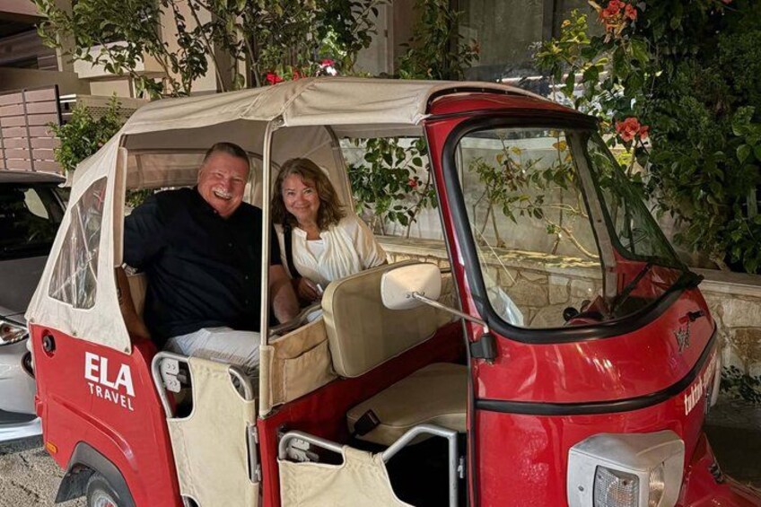 A red and beige car with 'ELA TRAVEL' on the side parked in front of a building with greenery. 5