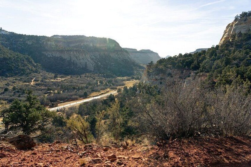 A mountainous landscape with a dirt road, dense vegetation, and a clear sky. 4