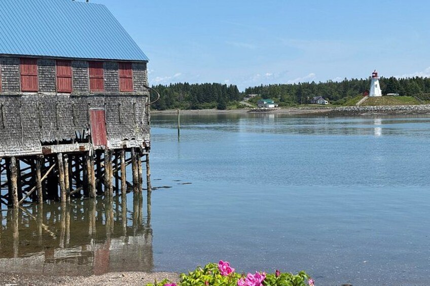 A wooden structure with a blue roof, a lighthouse, and a calm body of water. 1