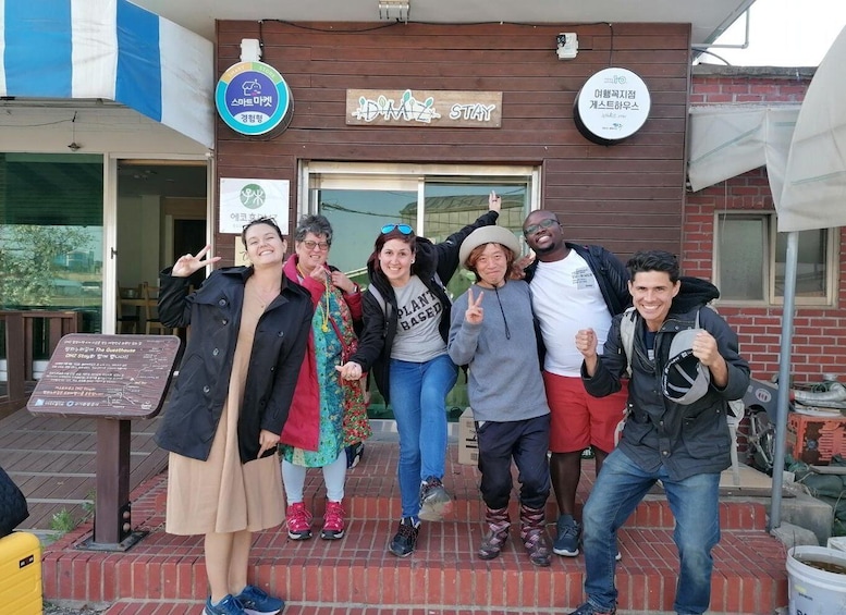 A group of people posing in front of a building with signs indicating a stay and a guesthouse. 1