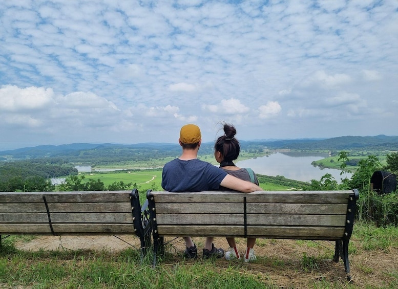 A couple sitting on a bench overlooking a lake and hills. 4