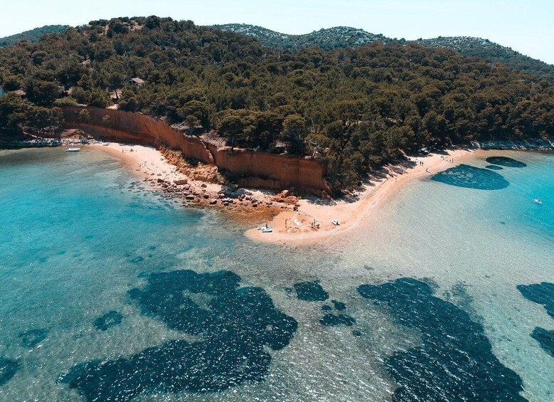 An aerial view of a coastal area with clear blue waters, a sandy beach, and a forested hill in the background. 3