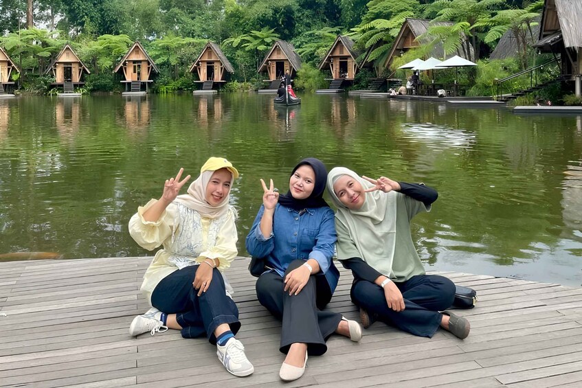Three people sitting on a wooden dock by a lake with floating houses in the background. 4
