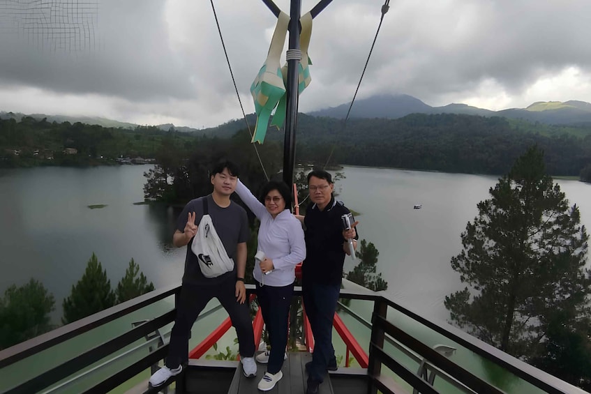 Three people on a cable car with a lake and mountains in the background. 5