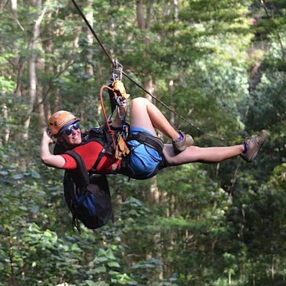 A person suspended in mid-air, wearing a helmet and harness, with a forested background. 1