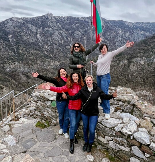 A group of people standing on a rocky mountain edge with a flag, surrounded by a mountainous landscape. 3