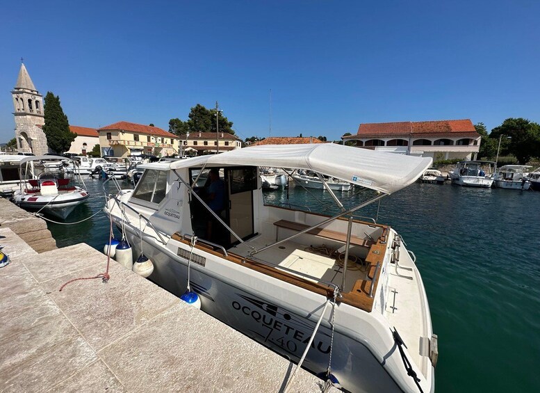 A marina with boats docked, a church tower, and buildings with red-tiled roofs. 2