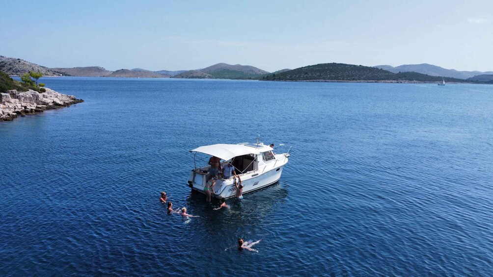 A boat with people swimming and standing around it on a calm lake surrounded by hills. 4