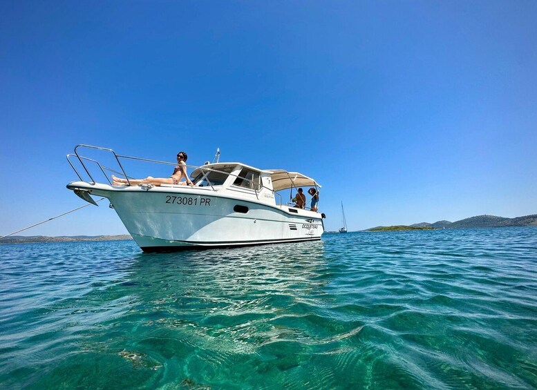 A white boat with the number 273081 PR on the bow, sailing on clear blue water with a distant shoreline. 1