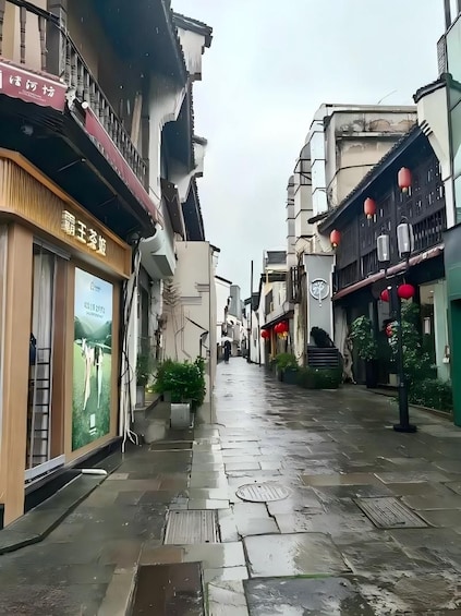 A narrow street with traditional architecture, wet pavement, and red lanterns. 1
