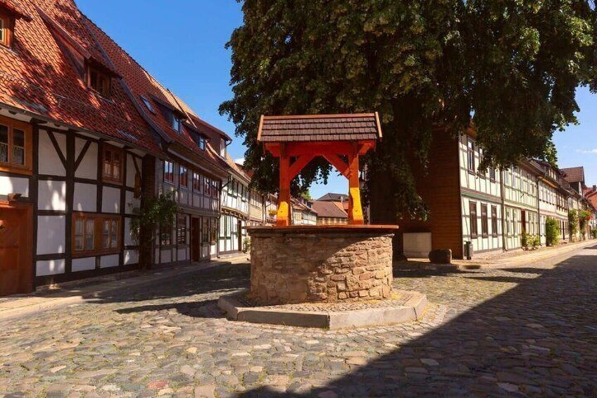 A cobblestone street with traditional half-timbered houses, a stone well, and a red-roofed structure. 4