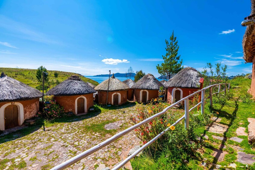 En rad traditionella hus med halmtak, mot en klarblå himmel och med en vattenyta i bakgrunden. 1