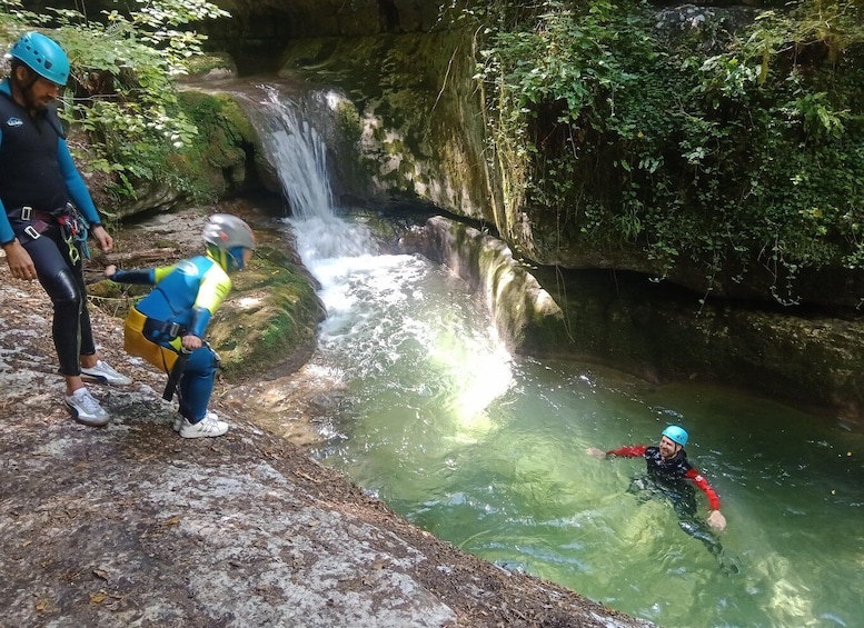 A person in a red wetsuit swimming in a clear river with a waterfall in the background. 3