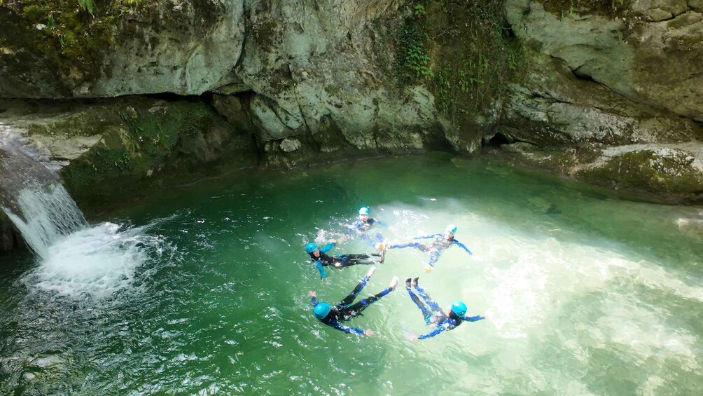 A group of people skydiving in a clear green body of water surrounded by rocky cliffs. 1