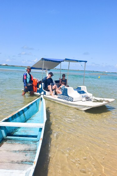 A small boat named 'MARESTOURS' with two people on board, another boat docked nearby, and a calm sea with a clear sky. 2