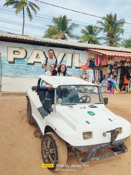 A white off-road vehicle parked in a sandy area with a mural in the background and a store selling hats and bags. 4