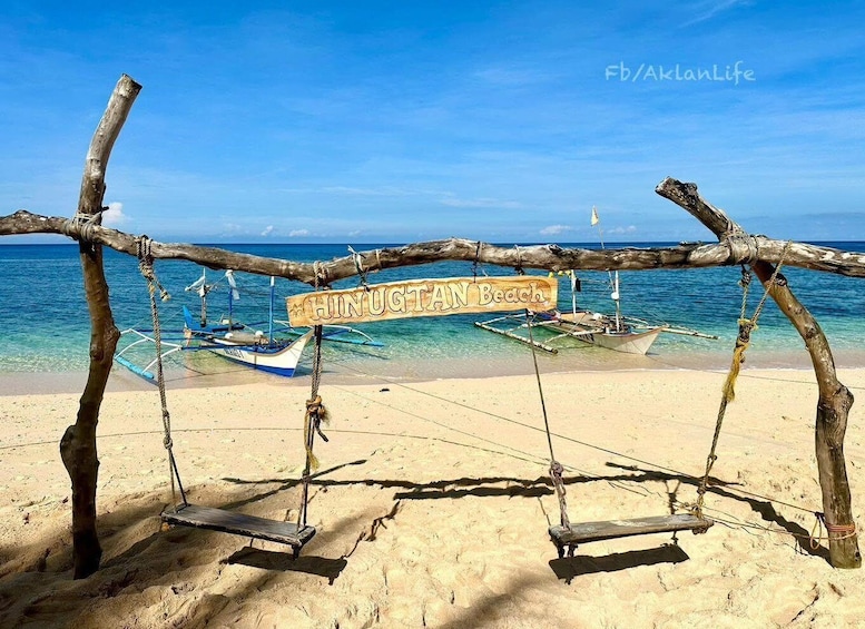 A beach with a swing set made of wooden logs and a sign that reads 'Hinugtan Beach'. 1