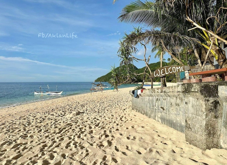 A sandy beach with footprints, a 'WELCOME' sign, palm trees, and a boat in the water. 5