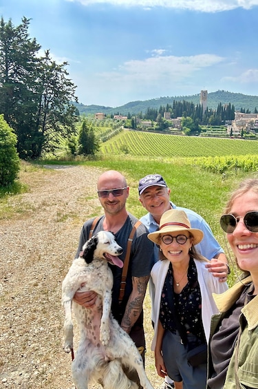 A group of people with a dog in a vineyard with rolling hills and a tower in the background. 3