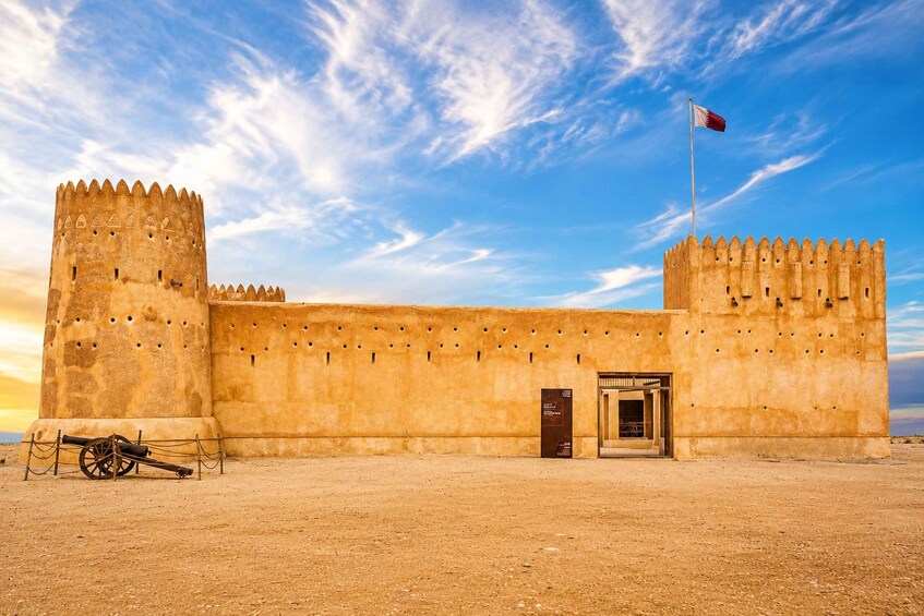A historic fort with a flag, a cannon, and a clear sky. 1