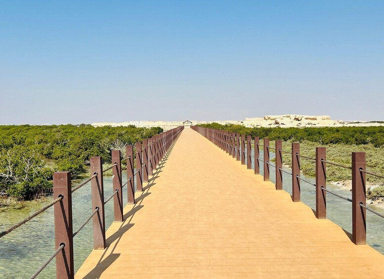 A long wooden bridge with metal railings, leading to a distant rocky landscape. 3