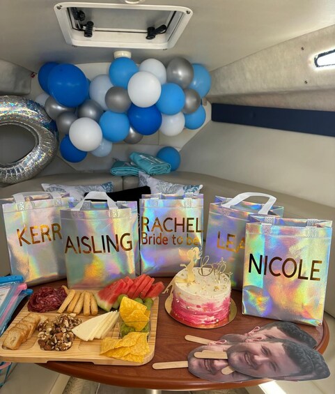 A table with food items, a cake, and gift bags with names on them. 5