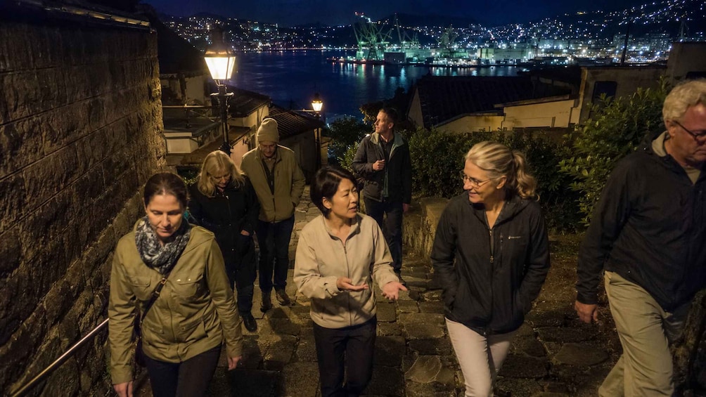 A group of people walking on a stone pathway at night, with a cityscape and a bridge in the background. 3