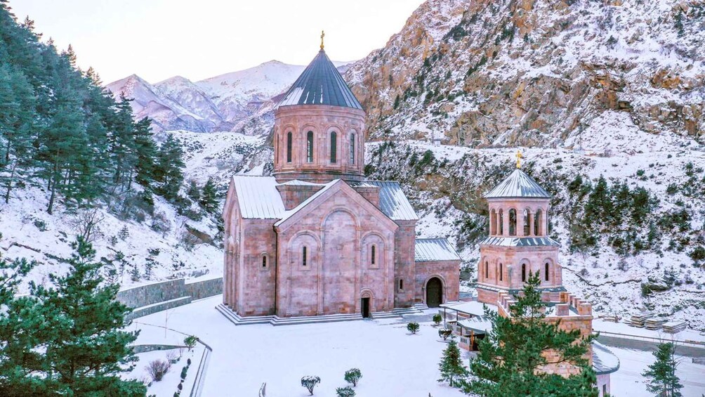 A snow-covered church with a bell tower and a smaller adjacent structure, surrounded by snow-laden trees and mountains. 4