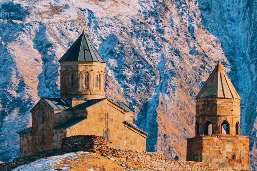 A stone church with a bell tower and a smaller adjacent structure, set against a mountainous backdrop. 5