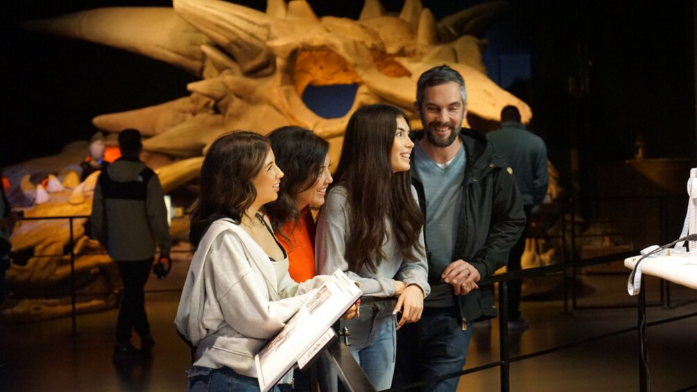 A group of people standing in a museum with a large dinosaur skeleton in the background. 1
