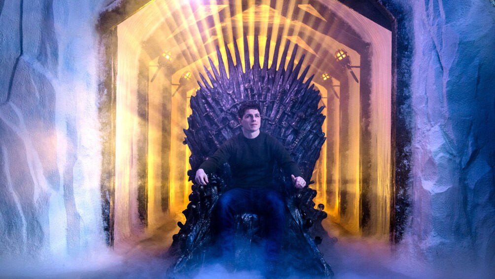 A person seated on a throne-like chair in a room with a golden archway and icy walls. 3