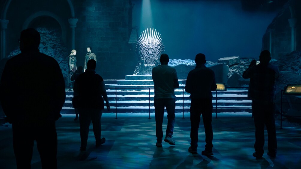 A group of people standing in a dimly lit room with a large, illuminated throne-like structure in the background. 4