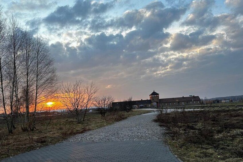 A pathway leading to a building with a tower, surrounded by bare trees and a cloudy sky. 2
