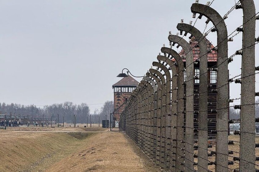 A long, curved concrete wall with barbed wire, a watchtower, and a barren landscape. 4