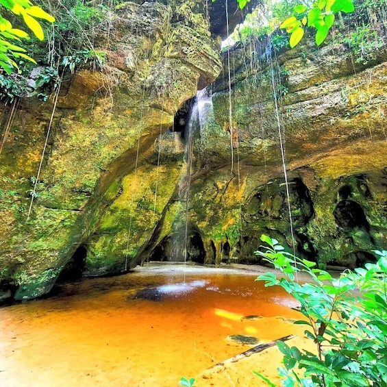 A cave with a waterfall, moss-covered rocks, and a pool of water. 1