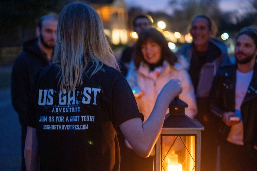 A person wearing a 'US GHOST Adventures' t-shirt, standing with a lantern. 5