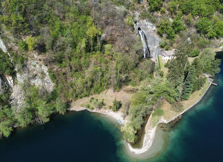An aerial view of a coastal area with a waterfall, dense forest, and a small house near the water's edge. 4