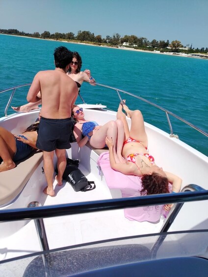 A boat with people sunbathing on the deck, surrounded by turquoise water and a distant shoreline with trees and buildings. 2