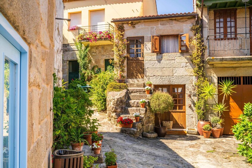 A narrow cobblestone alley with stone buildings, potted plants, and a small staircase leading to a door. 4