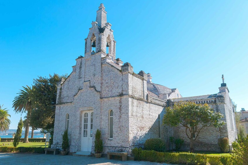 A historic stone church with a bell tower, surrounded by well-maintained gardens and palm trees. 5