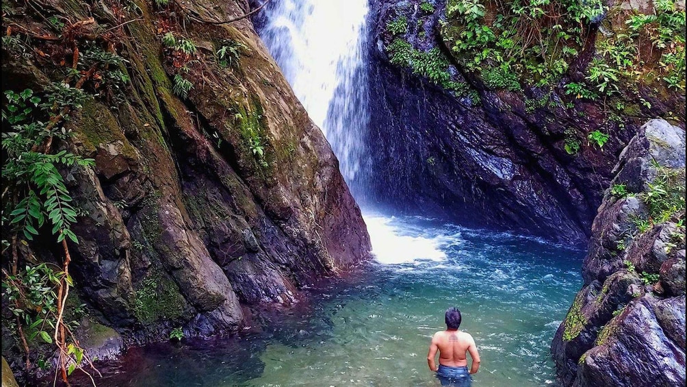 A waterfall in a rocky gorge with a person standing in the water. 1