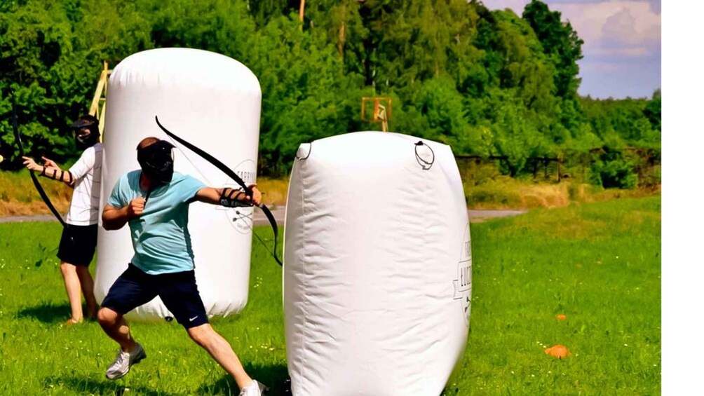 Two people playing paintball in an outdoor field with large white inflatable barriers. 1