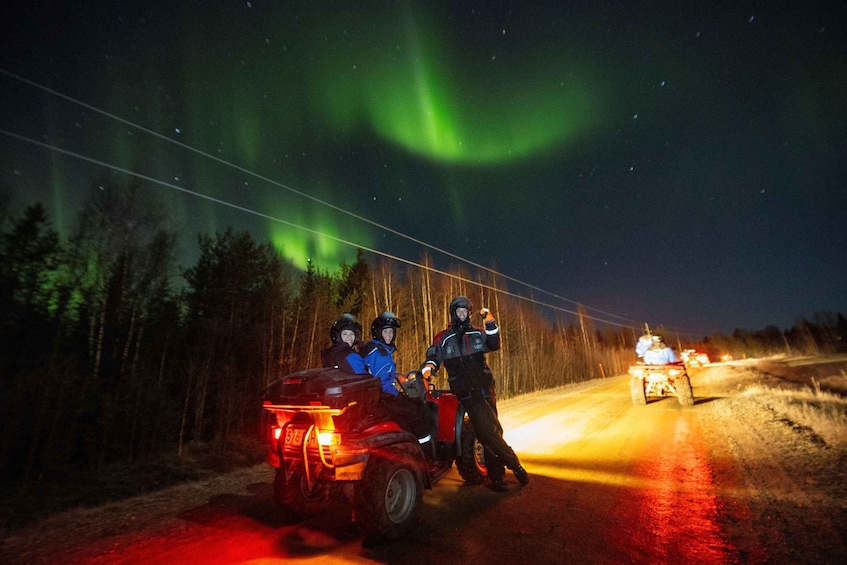 A group of people on a snowmobile, a road with lights, and the Northern Lights. 1