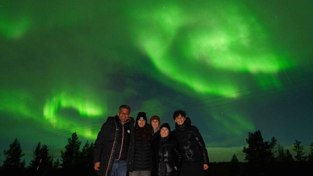 A group of people standing under a night sky with green aurora borealis. 2