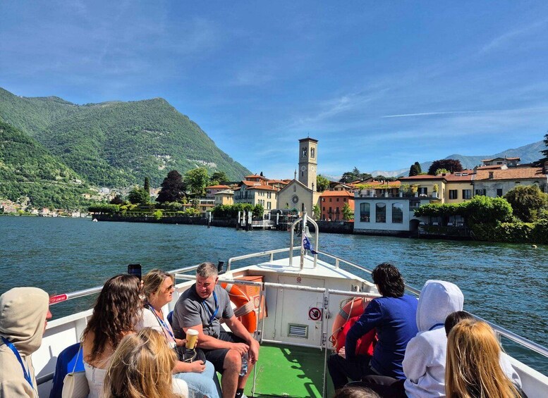 A boat with passengers looking at a town with a church tower across the water. 1