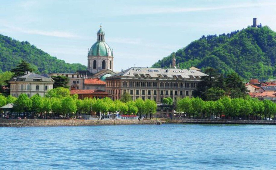 A historic building with a green dome, a river in the foreground, and a hill with trees in the background. 2