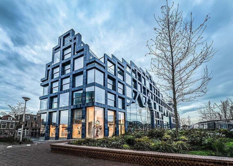 A modern building with a glass facade and a geometric design, surrounded by a landscaped area with trees and shrubs. 1