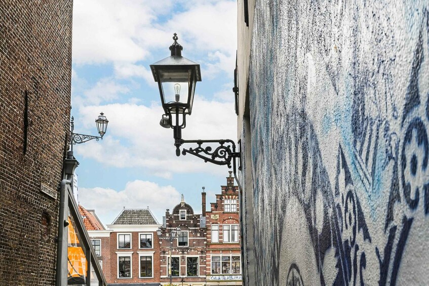 A narrow street with a street lamp, brick buildings, and a mural on the wall. 4