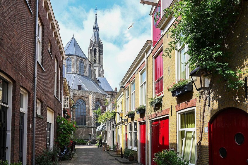 A narrow street with red doors and windows, a church with a tall spire, and a clear blue sky. 2